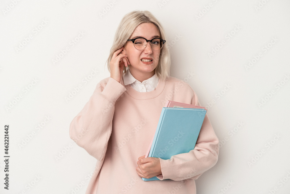 Young caucasian student woman holding books isolated on white background covering ears with hands.