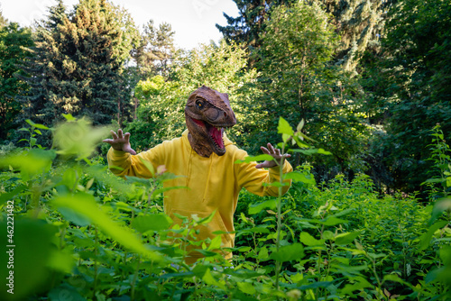 Boy wearing dinosaur mask while scaring amidst plants photo