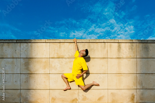 Man hanging on wall with one hand during sunny day