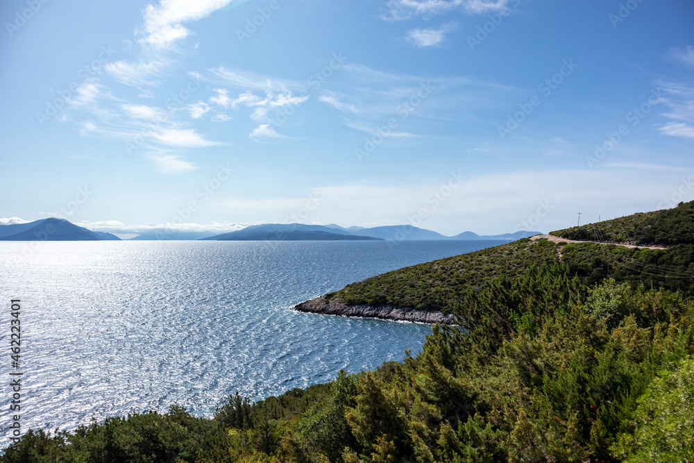 Green cliffs sunny sea shore on a bright clear blue day in Greece. Sun beam on water and blue sky, Lefkada island, Ionian sea coast