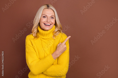 Photo of funny blond elder lady index empty space wear yellow sweater isolated on brown color background © deagreez