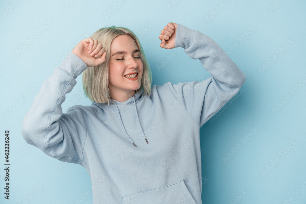 Young caucasian woman isolated on blue background celebrating a special day, jumps and raise arms with energy. Young caucasian woman isolated on blue background celebrating a special day, jumps and raise arms with energy.