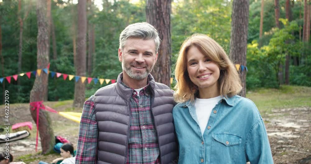 Portrait of male and female teachers standing in wood. Good looking people posing to camera and smiling with kids at the background. Close up of man and woman in park with smile on their face Portrait of male and female teachers standing in wood. Good looking people posing to camera and smiling with kids at the background. Close up of man and woman in park with smile on their face