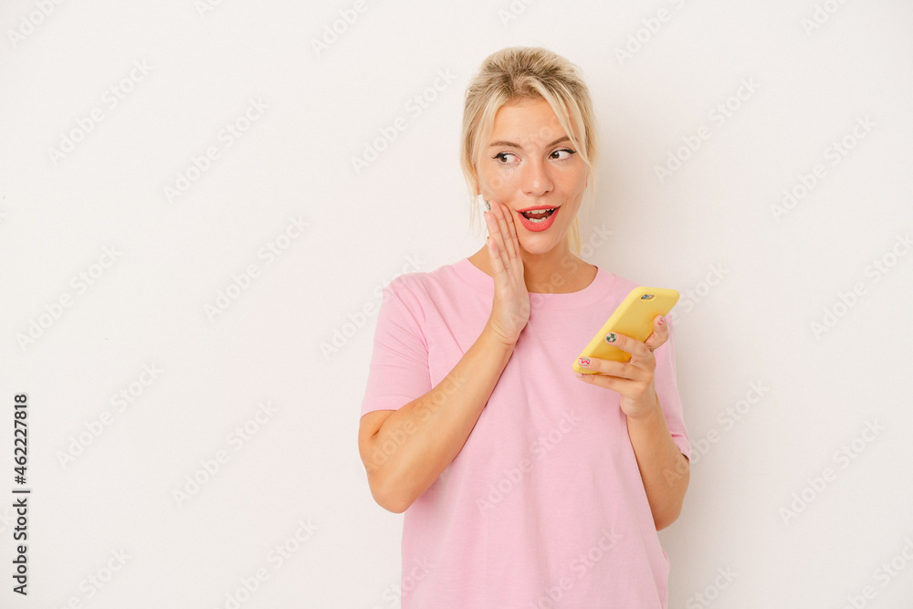 Young Russian woman holding mobile phone isolated on white background is saying a secret hot braking news and looking aside Young Russian woman holding mobile phone isolated on white background is saying a secret hot braking news and looking aside