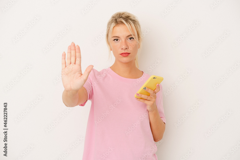 Young Russian woman holding mobile phone isolated on white background standing with outstretched hand showing stop sign, preventing you. Young Russian woman holding mobile phone isolated on white background standing with outstretched hand showing stop sign, preventing you.