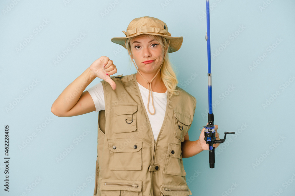 Young Russian fisherwoman isolated on blue background showing a dislike gesture, thumbs down. Disagreement concept. Young Russian fisherwoman isolated on blue background showing a dislike gesture, thumbs down. Disagreement concept.