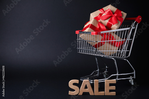 Cart with gift boxes and word Sale made of wooden letters on dark background, space for text. Black Friday