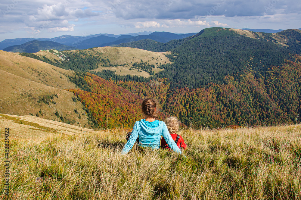 Happy mom and daughter sit on a mountainside in the Carpathians and admire the autumn forest Happy mom and daughter sit on a mountainside in the Carpathians and admire the autumn forest