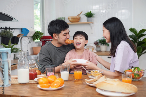 Asian family breakfast at home. Parents and children enjoy eating together  talking with laughter and good atmosphere. Father plays with son playfully at kitchen table.