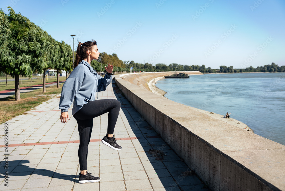 Young strong sexy muscular fit woman in doing high knee skip running in the place as hard outdoor workout training in the autumn cold and sunny weather as preparation for marathon race