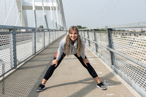 Young beautiful happy sporty fitness woman standing and stretching her muscles preparing for jogging and running exercise while she listening to music for workout and training motivation