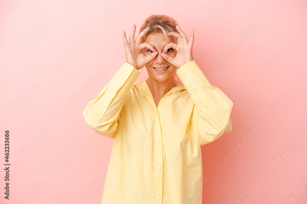 Young Russian woman isolated on pink background showing okay sign over eyes Young Russian woman isolated on pink background showing okay sign over eyes