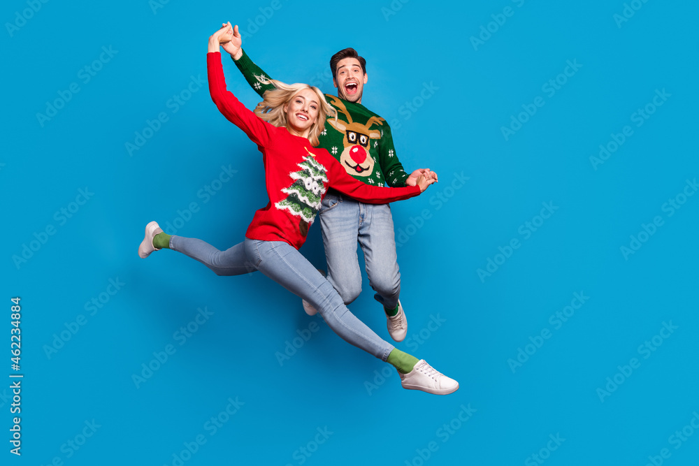 Full length body size photo couple holding hands jumping in ugly xmas sweater dancing isolated bright blue color background