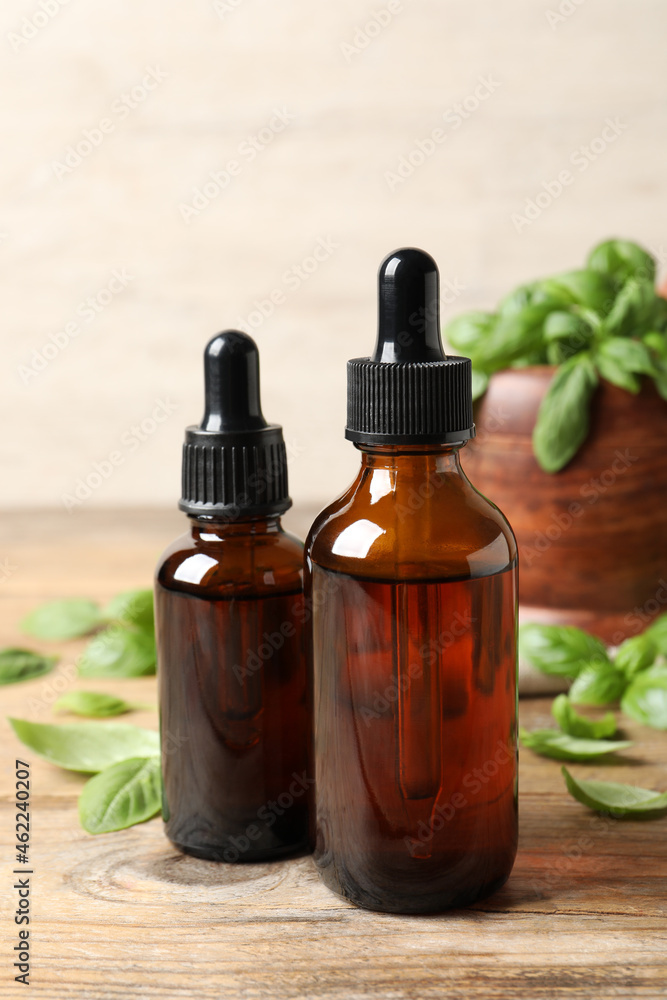 Bottles of basil essential oil and green leaves on wooden table Bottles of basil essential oil and green leaves on wooden table