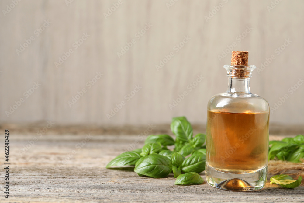 Glass bottle of basil essential oil and leaves on wooden table. Space for text Glass bottle of basil essential oil and leaves on wooden table. Space for text