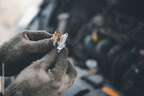фотографія Spark plug replacement work, Hand of the auto mechanic holding the old spark plug on blurred engine car on background