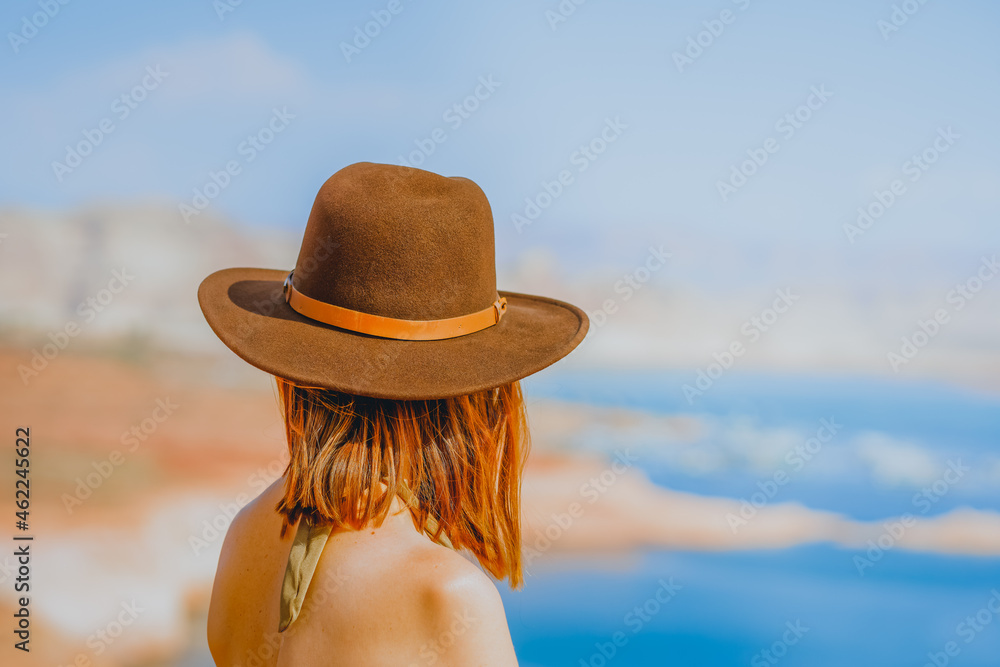 Red-haired woman wearing a hat on the beach overlooking lake
