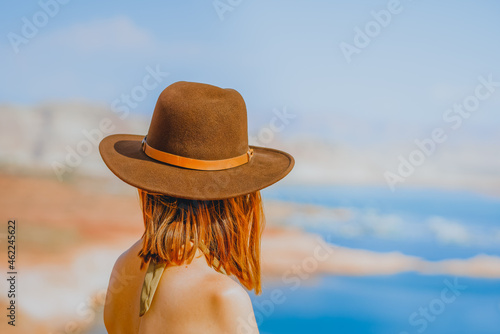 Red-haired woman wearing a hat on the beach overlooking lake