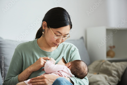 Asian young mother looking at her little child while she eating on her hands