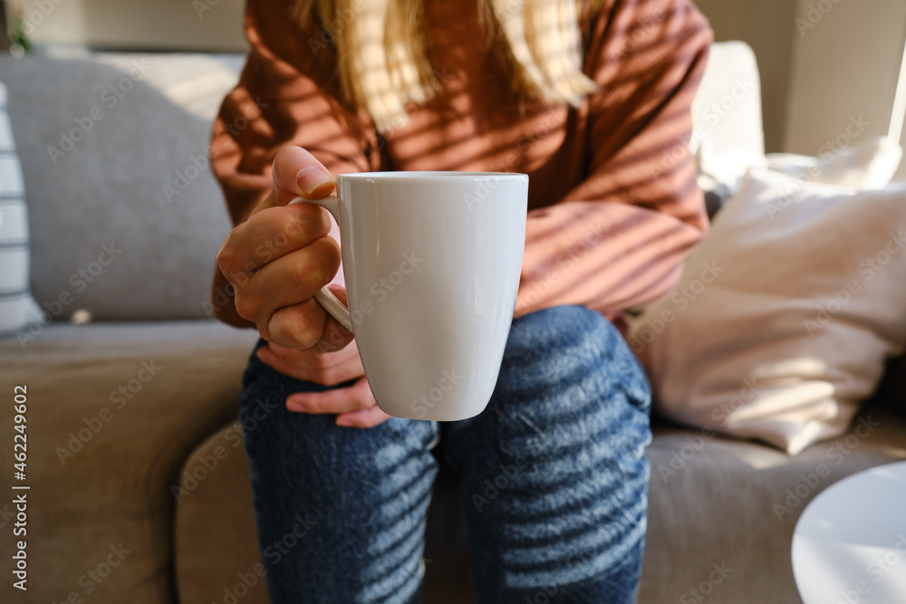 A cup of tea or coffee in the hands of a girl. In the morning, the girl drinks hot tea. Enjoy the comforts of home. White cup close-up in the hands of a woman in the rays of the sun from the window A cup of tea or coffee in the hands of a girl. In the morning, the girl drinks hot tea. Enjoy the comforts of home. White cup close-up in the hands of a woman in the rays of the sun from the window