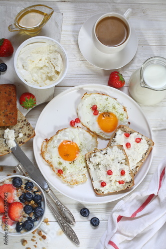Breakfast with scrambled eggs, muesli with fruits, berries and coffee with milk on a brown wooden background	