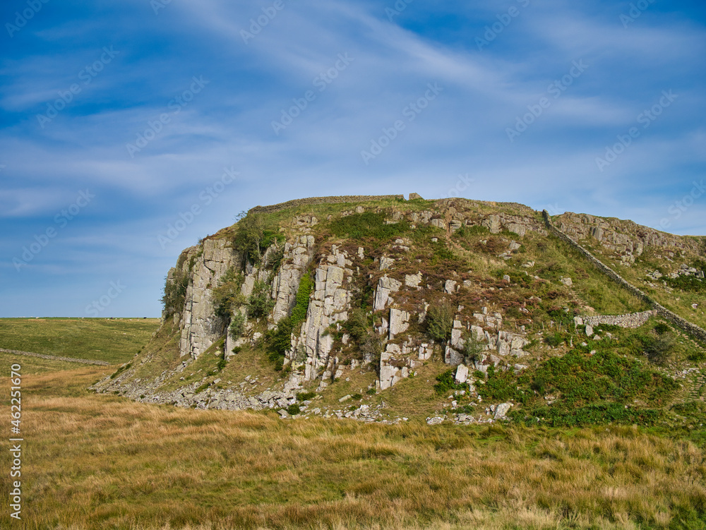 A rocky outcrop of the igneous rock dolerite on Hadriand's Wall Path in Northumberland, England, UK. The outcrop is part of the Great Whin Sill. Taken on a sunny day with blue sky and high clouds.
