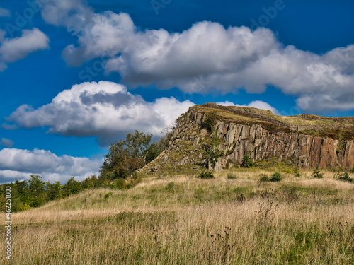 A rocky outcrop of the igneous rock dolerite at Walltown Country Park in Northumberland, England, UK. The outcrop is part of the Great Whin Sill. Taken on a sunny day with blue sky and white clouds. photo