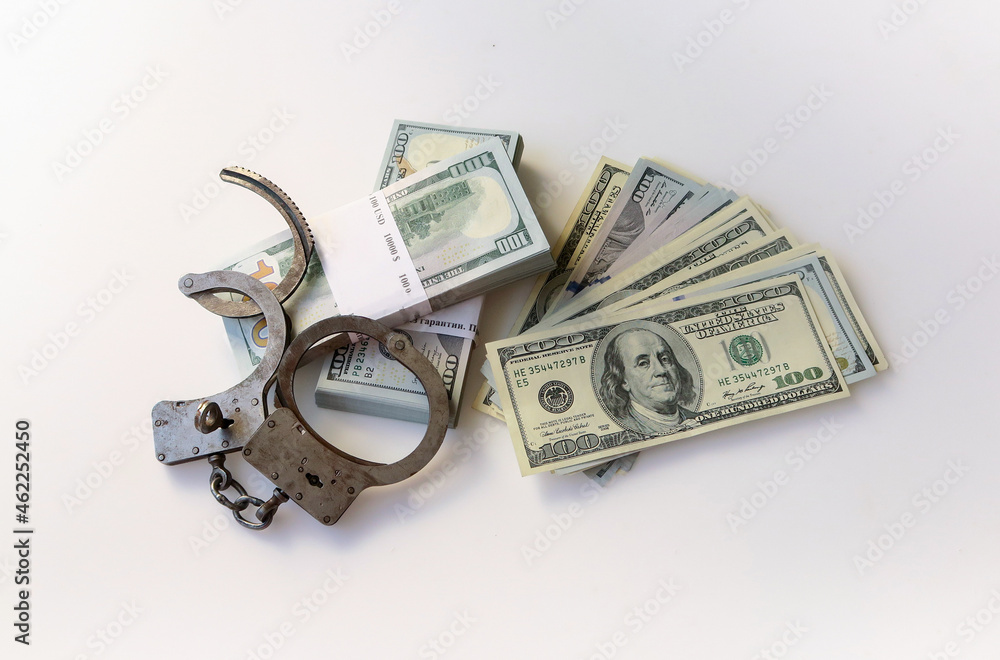 Police handcuffs on top of bundles of paper money on a white background. Twenty thousand American dollars. Police handcuffs on top of bundles of paper money on a white background. Twenty thousand American dollars.