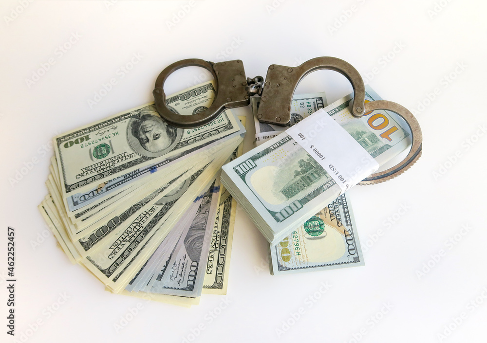 Police handcuffs on top of bundles of paper money on a white background. Twenty thousand American dollars. Police handcuffs on top of bundles of paper money on a white background. Twenty thousand American dollars.