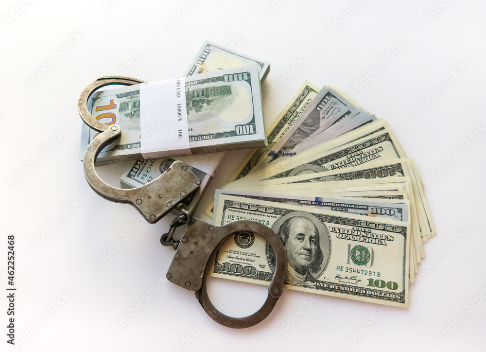 Police handcuffs on top of bundles of paper money on a white background. Twenty thousand American dollars. Police handcuffs on top of bundles of paper money on a white background. Twenty thousand American dollars.