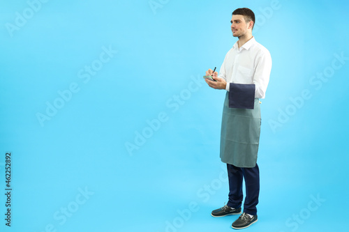 Waiter with notebook on blue background, space for text
