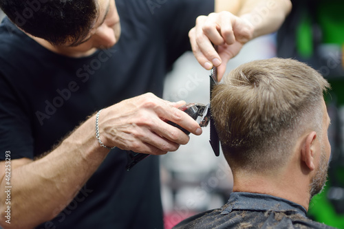 Barber master is shaving of handsome mature bearded man in salon. Hair artist making hairstyle for person in barbershop. Services of professional stylist.