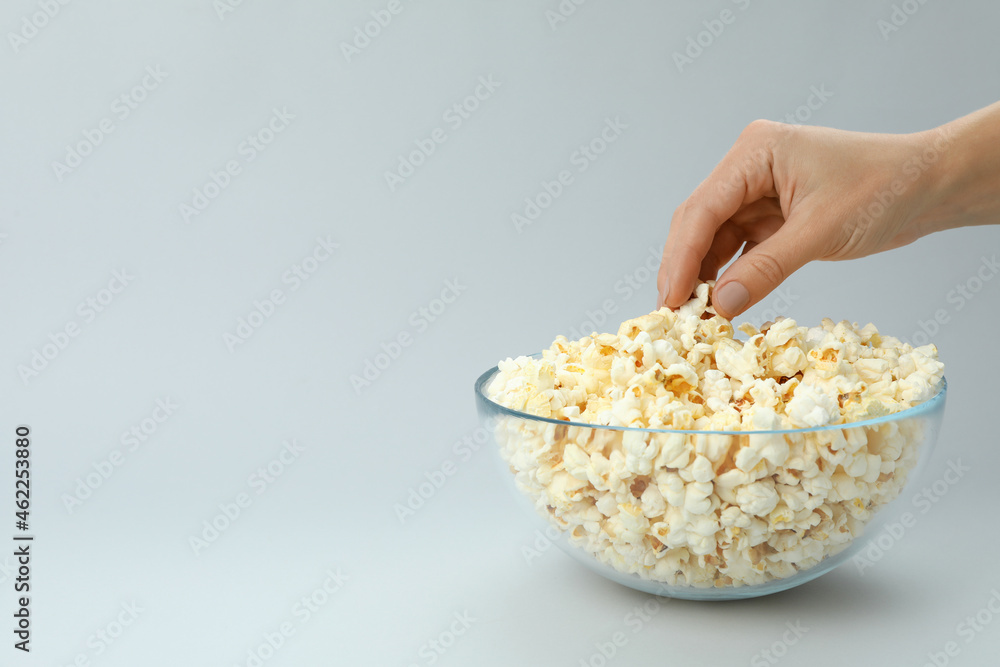 Female hand take popcorn from bowl on light gray background Female hand take popcorn from bowl on light gray background