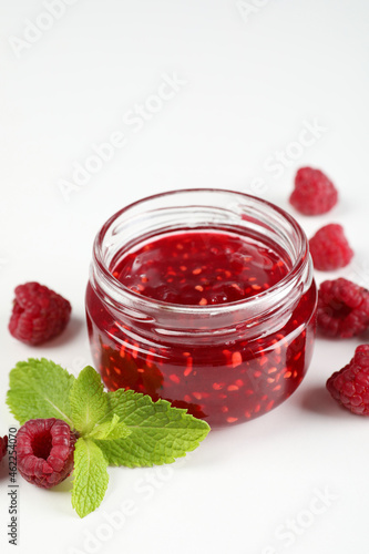 Jar of raspberry jam with ingredients on white background