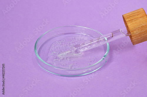 Pipette with dropper and wooden cover lies in the petri dish with cosmetics gel.Top view,liquid cosmetic,macro photography.Lilac banner with copy space.