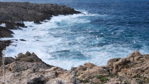 cliffs of Menorca, Spain. Waves of blue sea hurl themselves on the rocks.