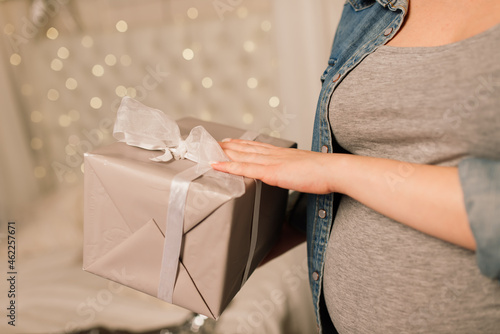 Close up of happy smiling pregnant woman touching her belly over christmas tree background