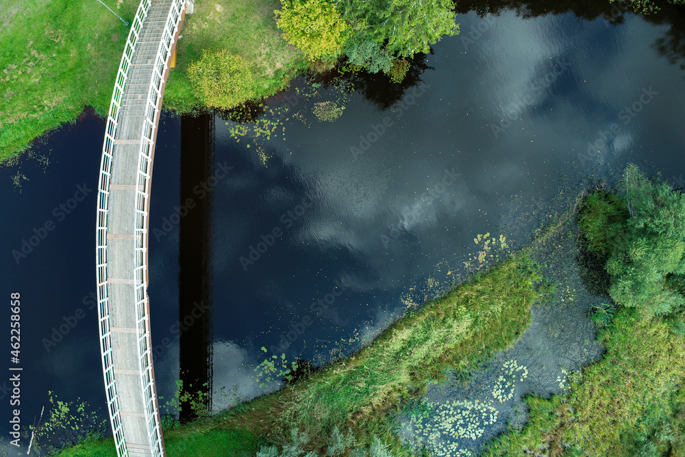 Arching bridge over a deep blue river in greenery - obrazy, fototapety, plakaty 