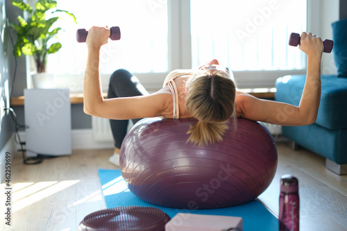 Foto Young woman lying on ball raises dumbbells up closeup