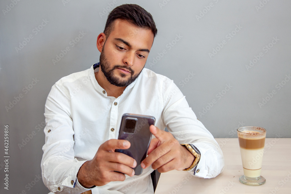 Hombre mirando el móvil. Chico chateando con el móvil. Hombre en cafetería con móvil. Hombre tomándose un café en la cafetería. Chico escribiendo con el móvil.
