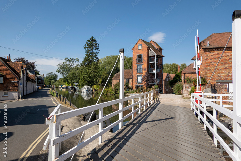 Fototapeta premium Newbury, Berkshire, England, UK. 2021. White wooden swing bridge over the Kennet and Avon Canal at Newbury, tall buildings a former granary. UK