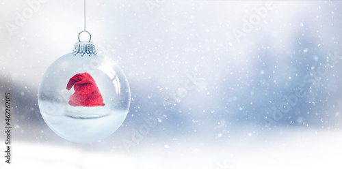 Gläserne Weihnachtskugel mit Weihnachtsmann vor unscharfem Blauem Hintergrund mit Schneeflocken