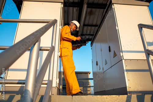 Male Electricity Engineer inspect and maintenance electric power system in generator at industrial plant. Technician writing, checklist work, and service on switchgear at substation control.