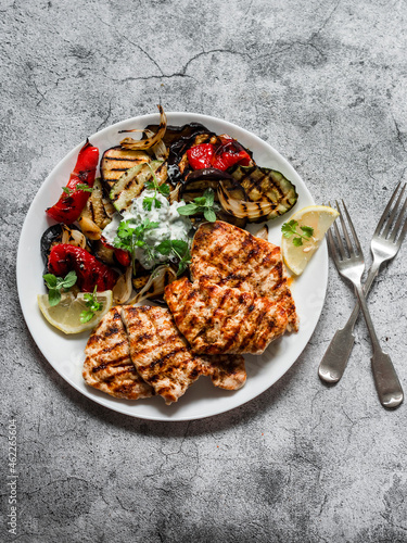 Delicious tapas barbecue plate - grilled turkey, eggplant, zucchini pepper with tzatziki sauce on a gray background, top view