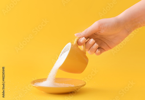 Woman sprinkling sugar from cup on color background