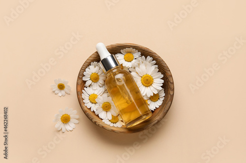 Bowl with chamomile flowers and bottle of essential oil on color background