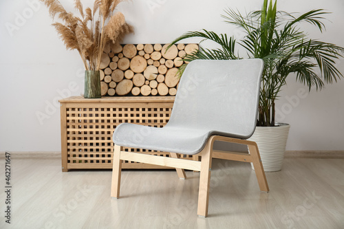 Modern armchair near wooden table with decor and dry reed in living room