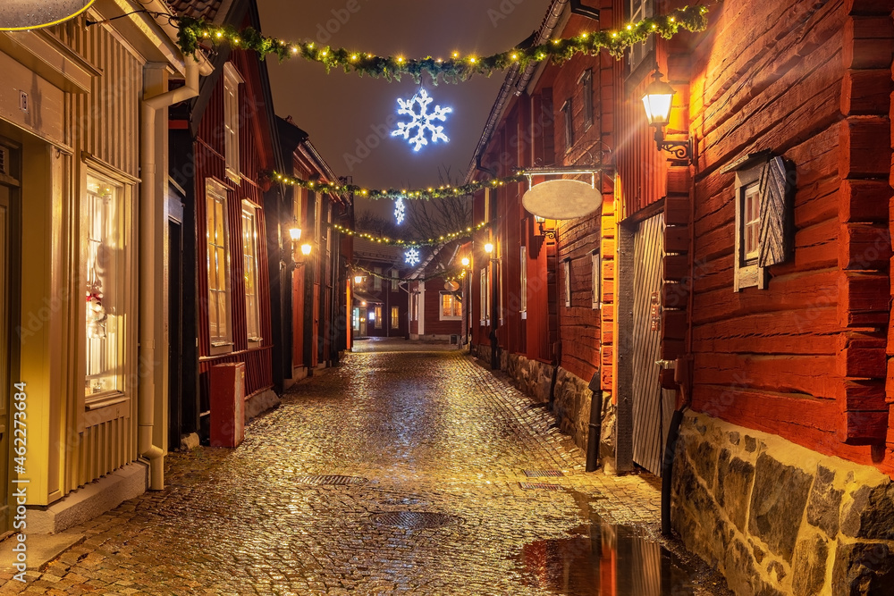 A narrow street with Scandinavian traditional  red wooden houses and coblestone pavement decorated with Christmas lights. Ideal to promote tourist destinations and illustrate certain seasons