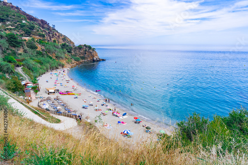 Fototapeta Naklejka Na Ścianę i Meble -  Pequeña cala en forma de herradura con acantilados a su espalda un día soleado de verano en época de vacaciones un día soleado con cielo azul. Desde Maro, Nerja, Málaga, Andalucía, España.