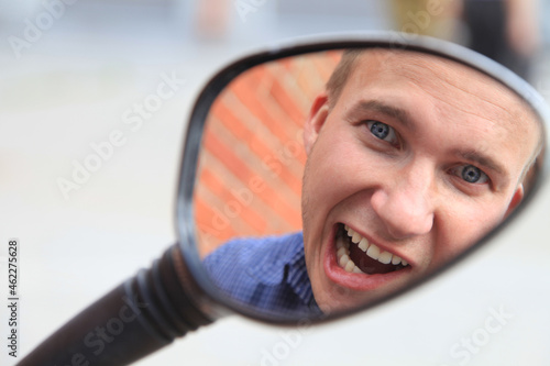 Portrait of a man in a mirror image.A comical, cheerful, cheerful guy in the mirror from a motorcycle. High quality photo